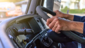 Truck driver gripping steering wheel inside commercial vehicle cab on city road