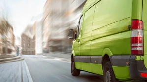 Green commercial delivery van speeding through urban street in motion blur