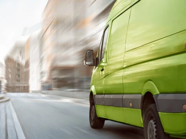 Green commercial delivery van speeding through urban street in motion blur