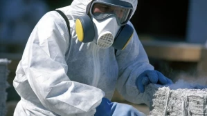 Hazmat worker in protective suit handling asbestos materials at industrial site