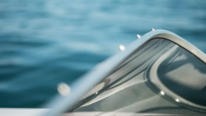 Close-up detail of a sleek motorboat windshield and chrome hull reflecting sunlight on calm open water, used in boating accident attorney website imagery