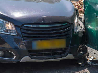 A car with a busted fender due to a bus crash with a green city bus.
