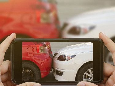 A person at the scene of a car accident photographs the damage with a cell phone camera.
