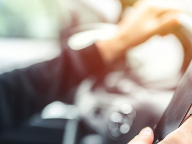 A driver engages in distracted driving by holding up a cell phone while steering the car.