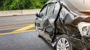 Black car with severe side panel damage after a rear-end collision on a highway, illustrating the property damage and injuries sustained in car accidents