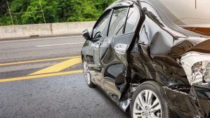 Black car with severe side panel damage after a rear-end collision on a highway, illustrating the property damage and injuries sustained in car accidents