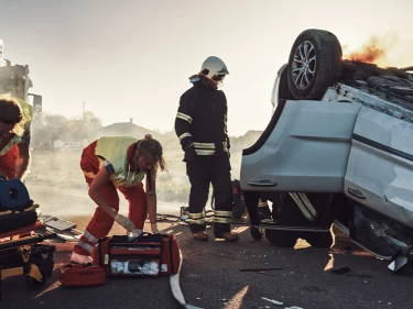Emergency responders treating an injured victim on a stretcher beside an overturned burning vehicle, representing the life-altering injuries in serious car accident cases