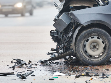 Car with completely destroyed front end surrounded by debris on a foggy road, illustrating the severe vehicle damage used to calculate car accident claim values