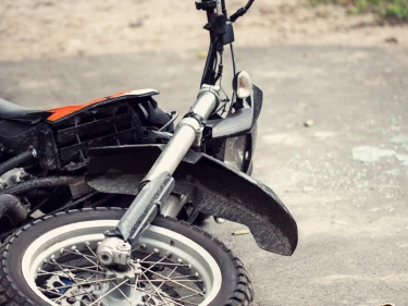 Crashed dirt bike lying on road with broken front fork and shattered debris nearby