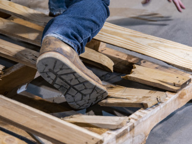 Person falling through broken wooden pallet on warehouse floor in workplace slip and fall accident