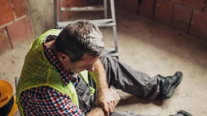Injured construction worker in safety vest sitting on floor clutching knee after workplace accident