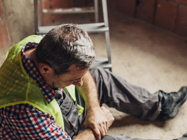 Injured construction worker in safety vest sitting on floor clutching knee after workplace accident