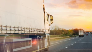 White semi-truck passing at high speed on busy highway at orange sunset