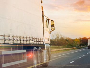 White semi-truck passing at high speed on busy highway at orange sunset