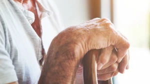 Elderly man hands resting on wooden walking cane representing long-term personal injury and mobility loss