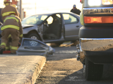 Firefighter working at the scene of a multi-vehicle crash with an ambulance and damaged cars in the background, representing the serious injuries that follow car accidents