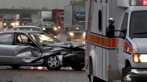Severely damaged silver car on a rainy highway with an ambulance responding, representing the serious injuries sustained in wet weather car accidents