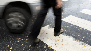 Pedestrian stepping into crosswalk as car speeds past on a rainy street, depicting a near pedestrian accident