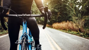 close-up front view of cyclist on blue road bike riding through wooded road at sunrise