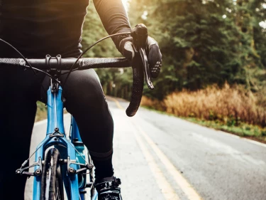 close-up front view of cyclist on blue road bike riding through wooded road at sunrise