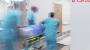 Medical team in teal scrubs rushing gurney past emergency room sign in hospital corridor