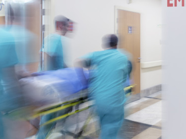 Medical team in teal scrubs rushing gurney past emergency room sign in hospital corridor