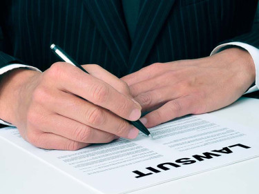 A lawyer for motorcycle accident injuries sits at a table in a dark suit with a pen in his hand as he prepares the paperwork for a lawsuit.