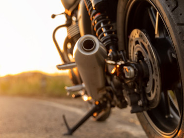 Motorcycle rear tire, exhaust pipe, and kickstand parked on roadside at sunset