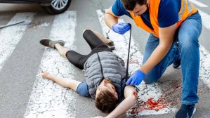 Emergency responder in safety vest aiding injured pedestrian lying in crosswalk after a vehicle accident