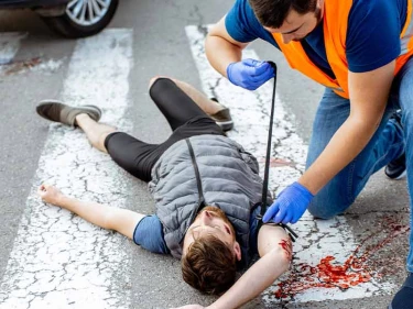 Emergency responder in safety vest aiding injured pedestrian lying in crosswalk after a vehicle accident