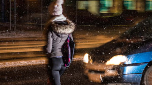 Dressed in a coat and winter hat, a woman is seconds away from being injured in a pedestrian accident as she crosses the street at night in front of a car.