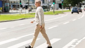 Older man crossing a wide urban street at a marked crosswalk with traffic light, illustrating pedestrian safety rights