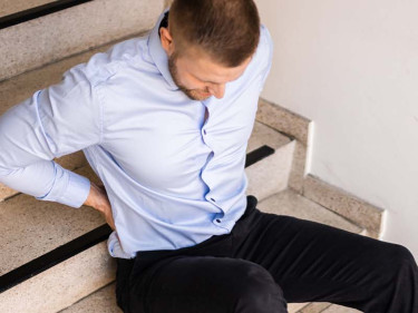 Man seated on stairs clutching lower back after slip and fall accident causing injury
