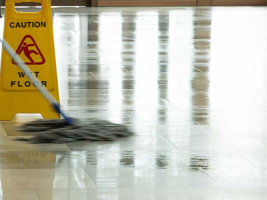 Janitor mopping shiny tile floor beside wet floor warning sign creating slip and fall risk