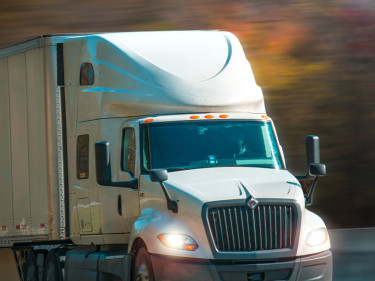 White International semi-truck with headlights on traveling at speed on Texas highway