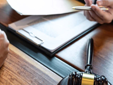 A client with folded hands sits at a desk across from a truck wreck attorney holding a pen and paper.