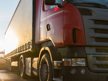 Large red commercial semi-truck with flatbed trailer parked at Texas trucking yard at sunset
