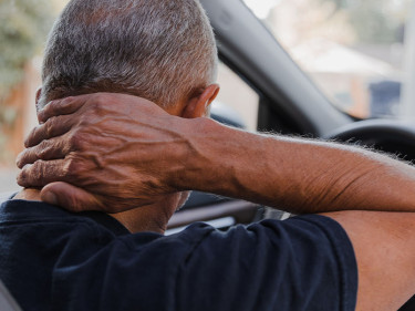 Driver clutching neck from behind in vehicle representing whiplash injury after a car accident