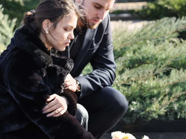 A young man and woman dressed in black place flowers on a grave, representing the outcome of common wrongful death examples.