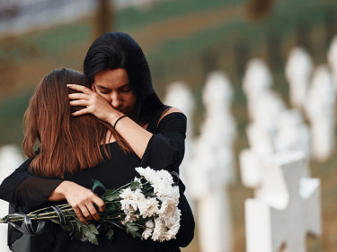 Two grieving women embracing at a cemetery after a wrongful death.